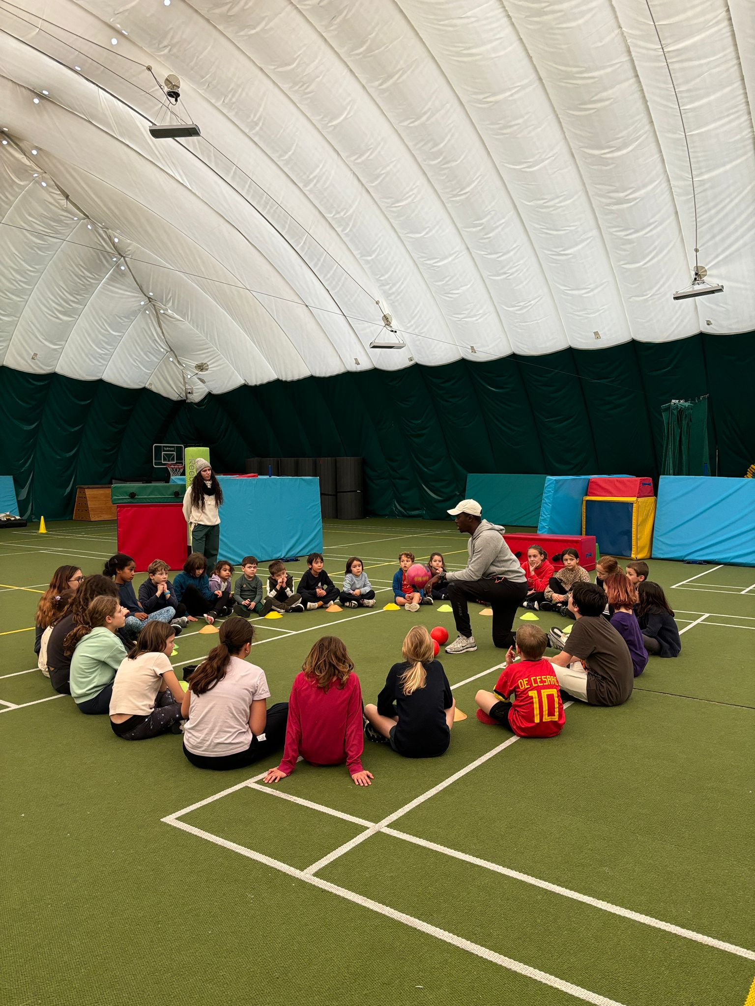 Photo of a group of young children sitting in circles around a facilitator in a gymnasium